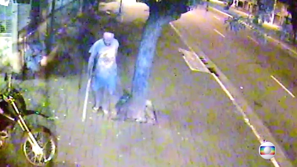 Agressor, com pedaço de pau na mão, caminha na rua após espancar Valdiram. Crédito: Reprodução/TV Globo